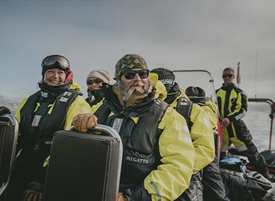 Happy guests on board a RIB boat during a trip, wearing flotation suits and life jackets