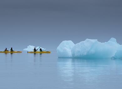 Three kayaks with guests paddling between nearby floating icebergs