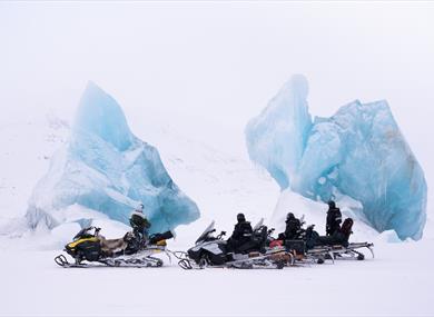 A guide and guests with snowmobile taking a break next to two large icebergs frozen in sea ice