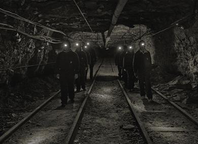 A group of guests with head lamps and helmets on, walking through a mine passage on a guided tour