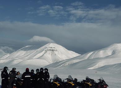 A group of people are standing in the winter landscape around snowmobiles