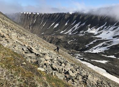 A person on the way up the side of Sarkofagen by foot together with a dog