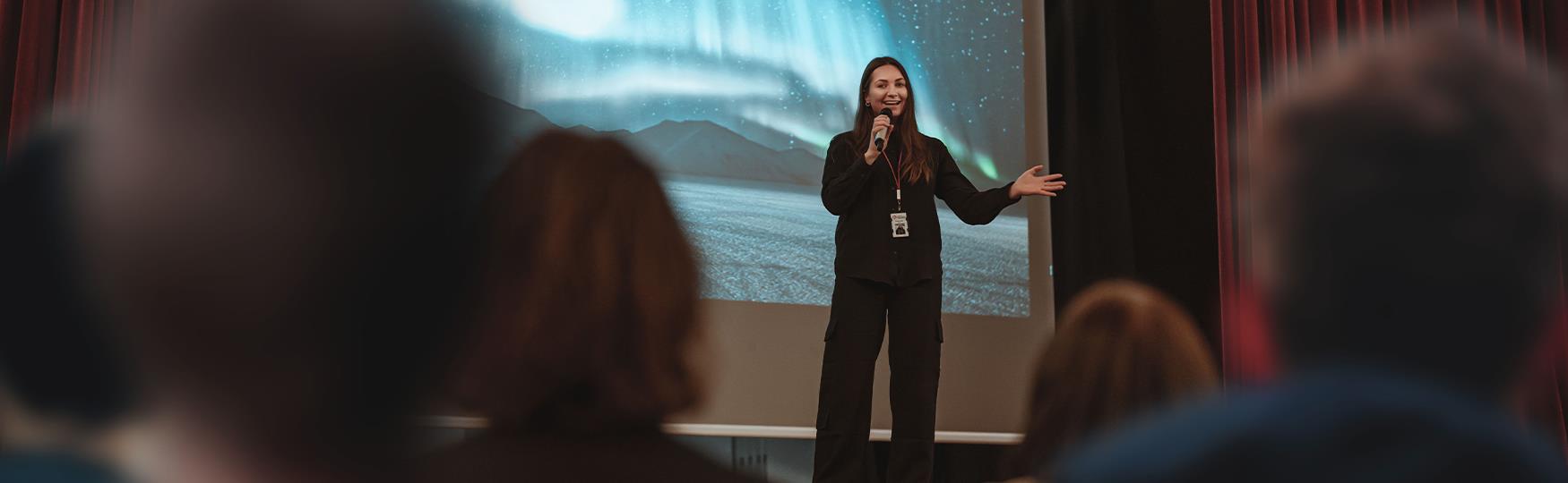 A person on a stage talking to a group of people in the foreground