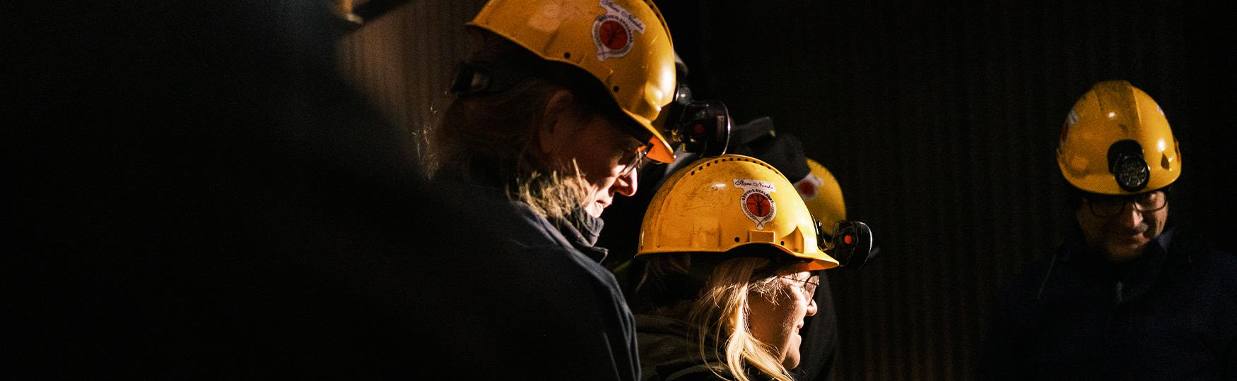 Personer i en mørk gruve som har på seg gule gruvehjelmer