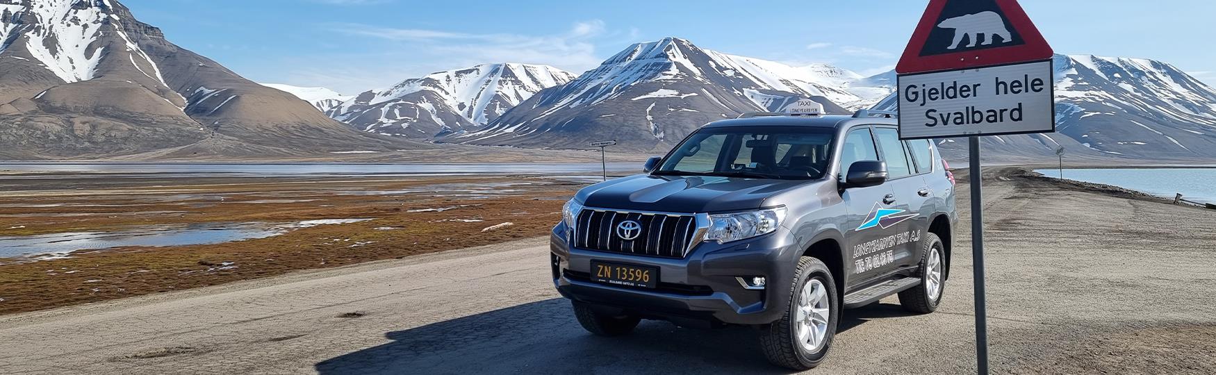 A taxi parked next to a polar bear warning sign along a road with a mountainous landscape in the background