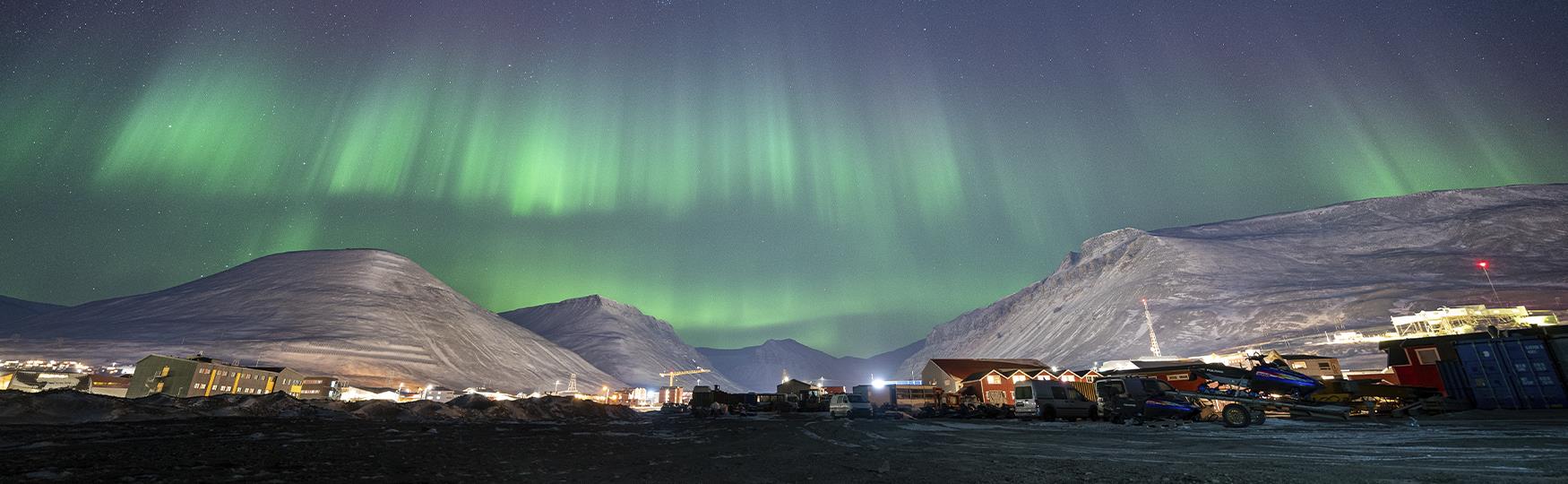 Et bylandskap med snødekte fjell og nordlys på en mørk himmel i bakgrunnen