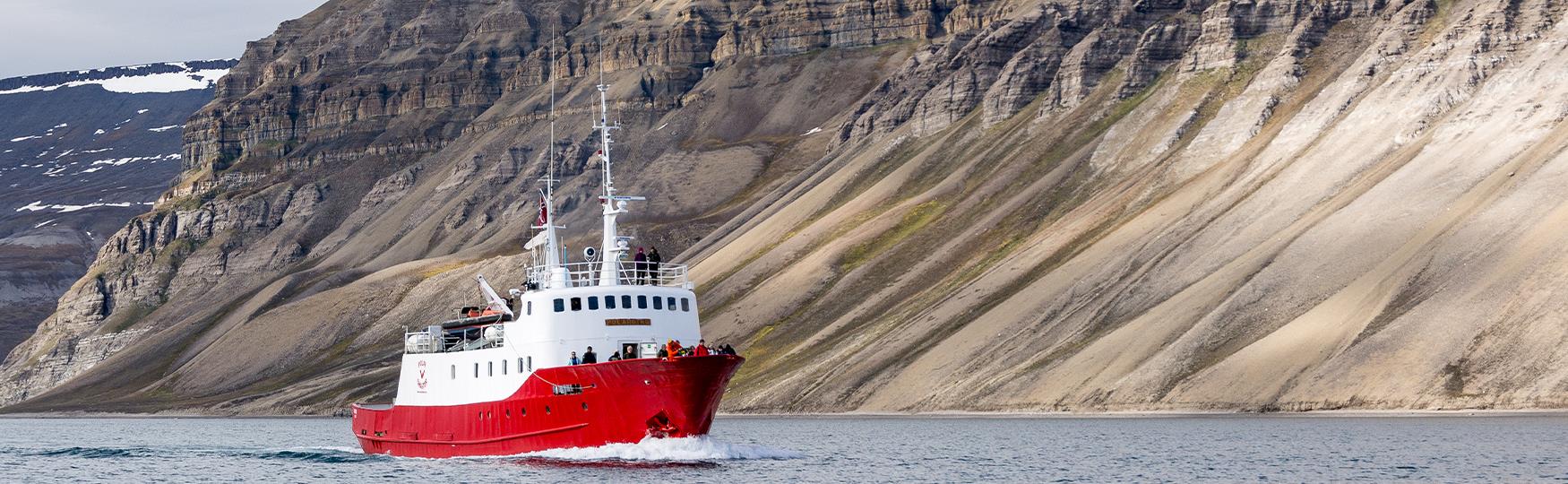 En båt som seiler langs en fjellrekke med gjester om bord