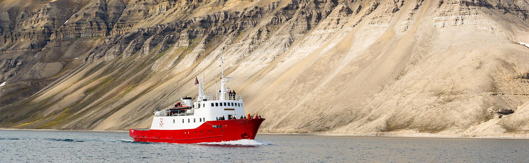 A boat sailing through a fjord alongside a mountain range