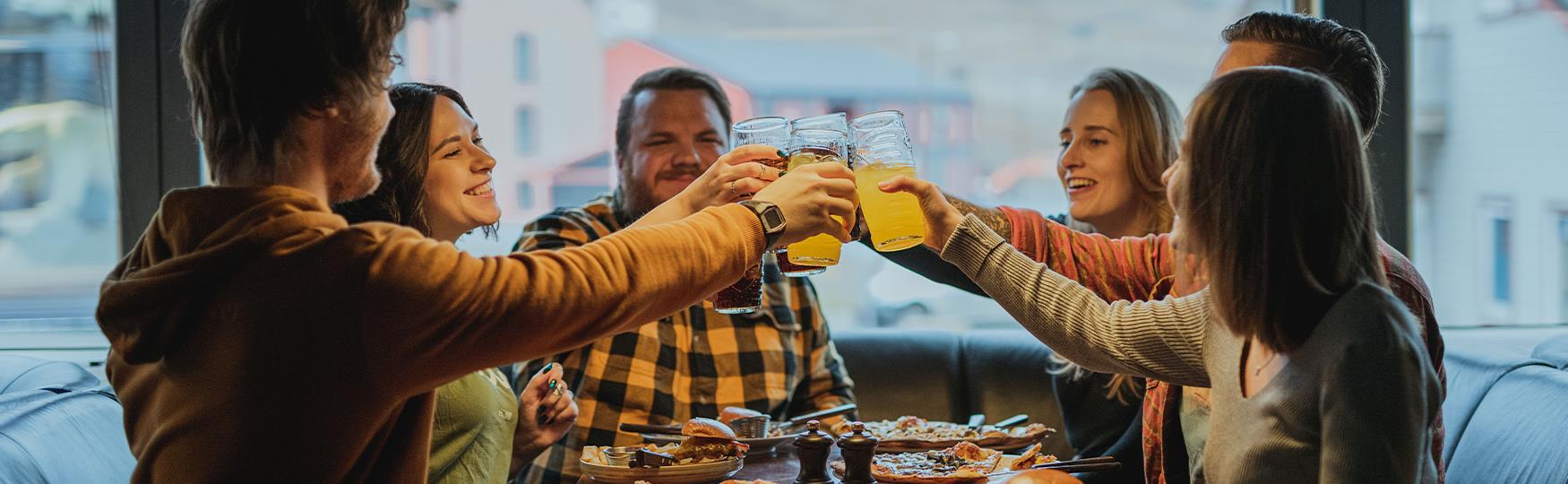 A group of people sitting around a table cheering with their glasses over a table filled with food