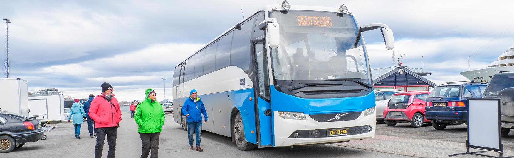 A sightseeing bus in a parking lot with people walking alongside it