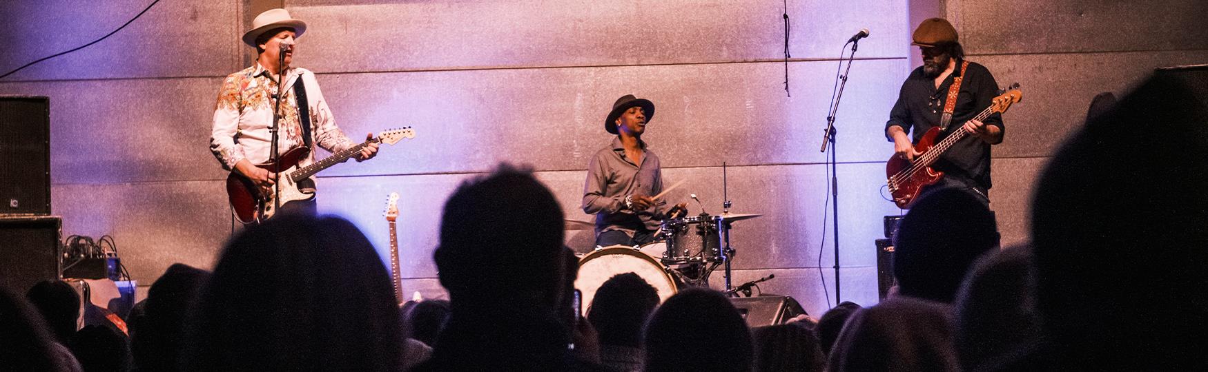 A band on a stage with an audience in silhouette in the foreground