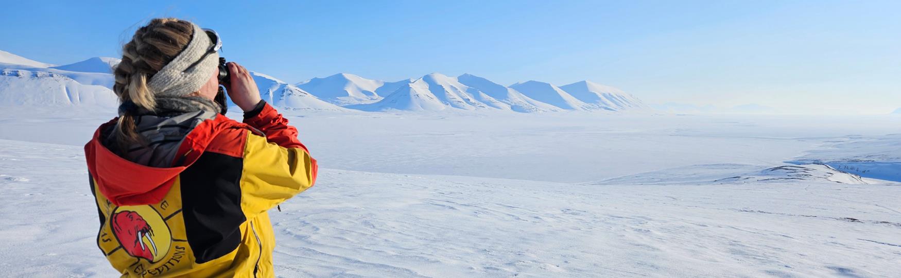 A guide looking through binoculars at white snowcovered fields