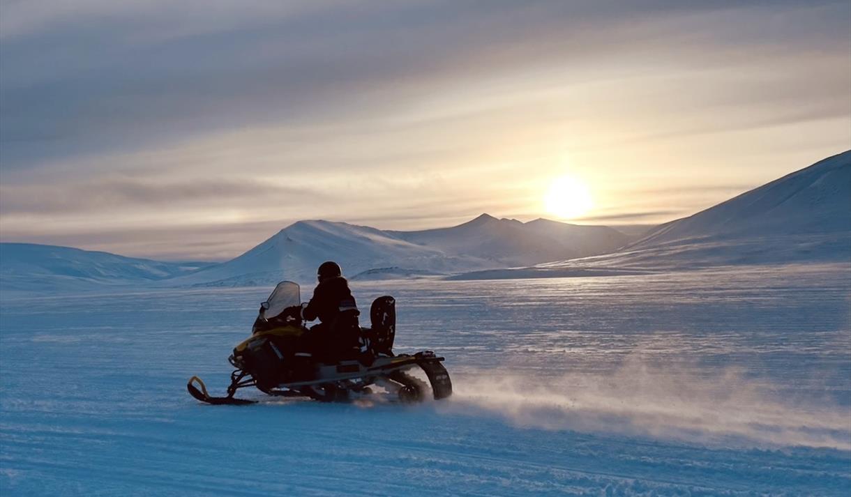 Snøscooter som kjører med sol og fjell i bakgrunnen