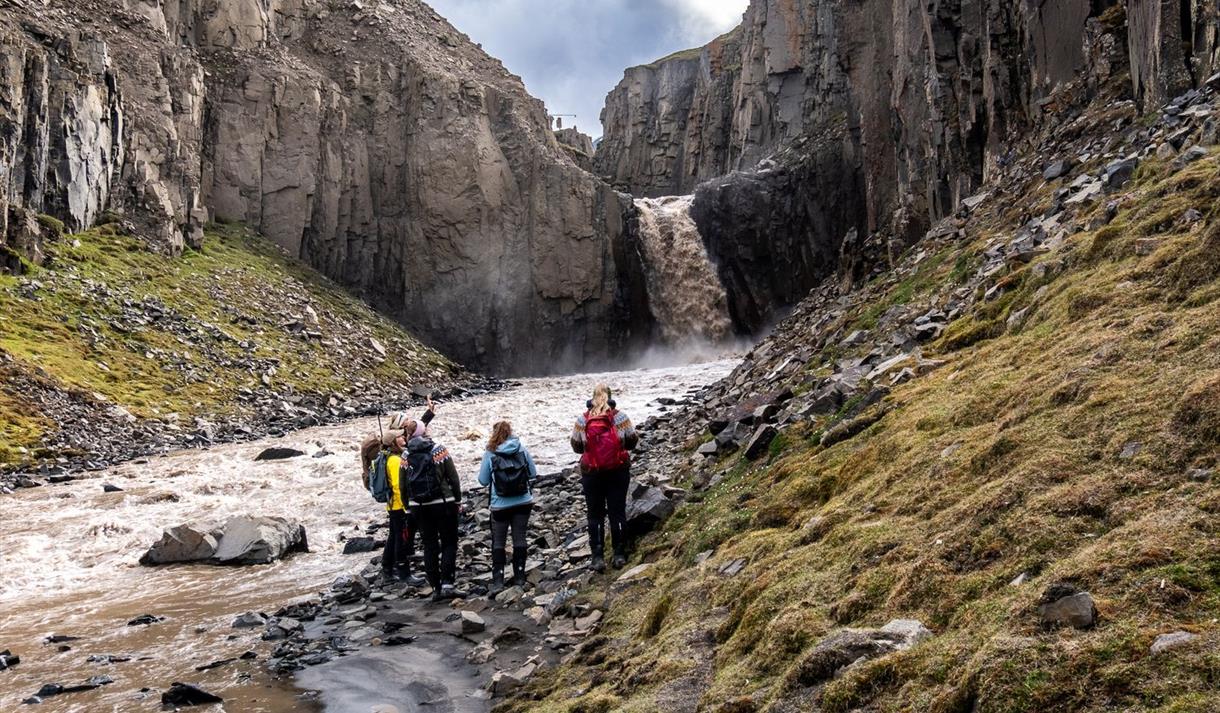 Turgruppe står ved en elv i en kløft. Fossefall i bagrunnen.