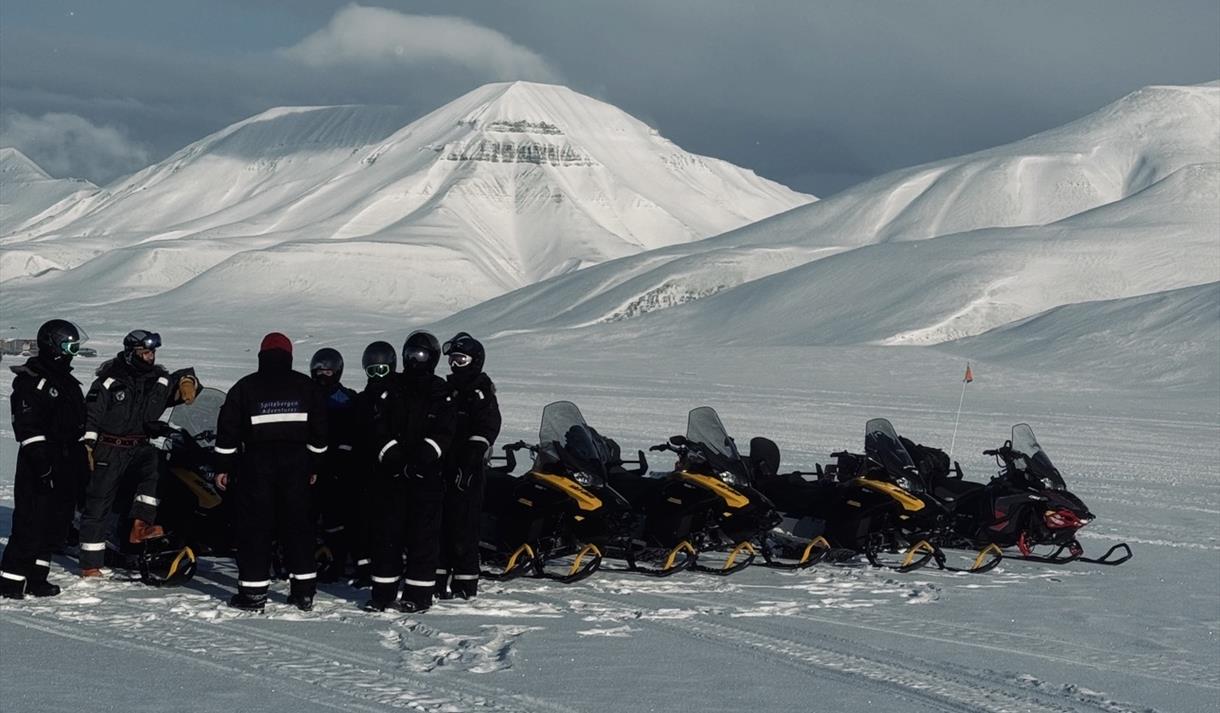 A group of people are standing in the winter landscape around snowmobiles
