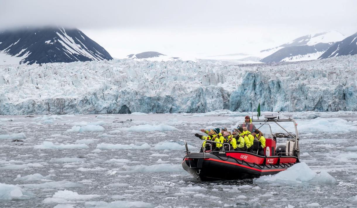 Several people in open RIB boat in front of glacier. The fjord is full of ice.