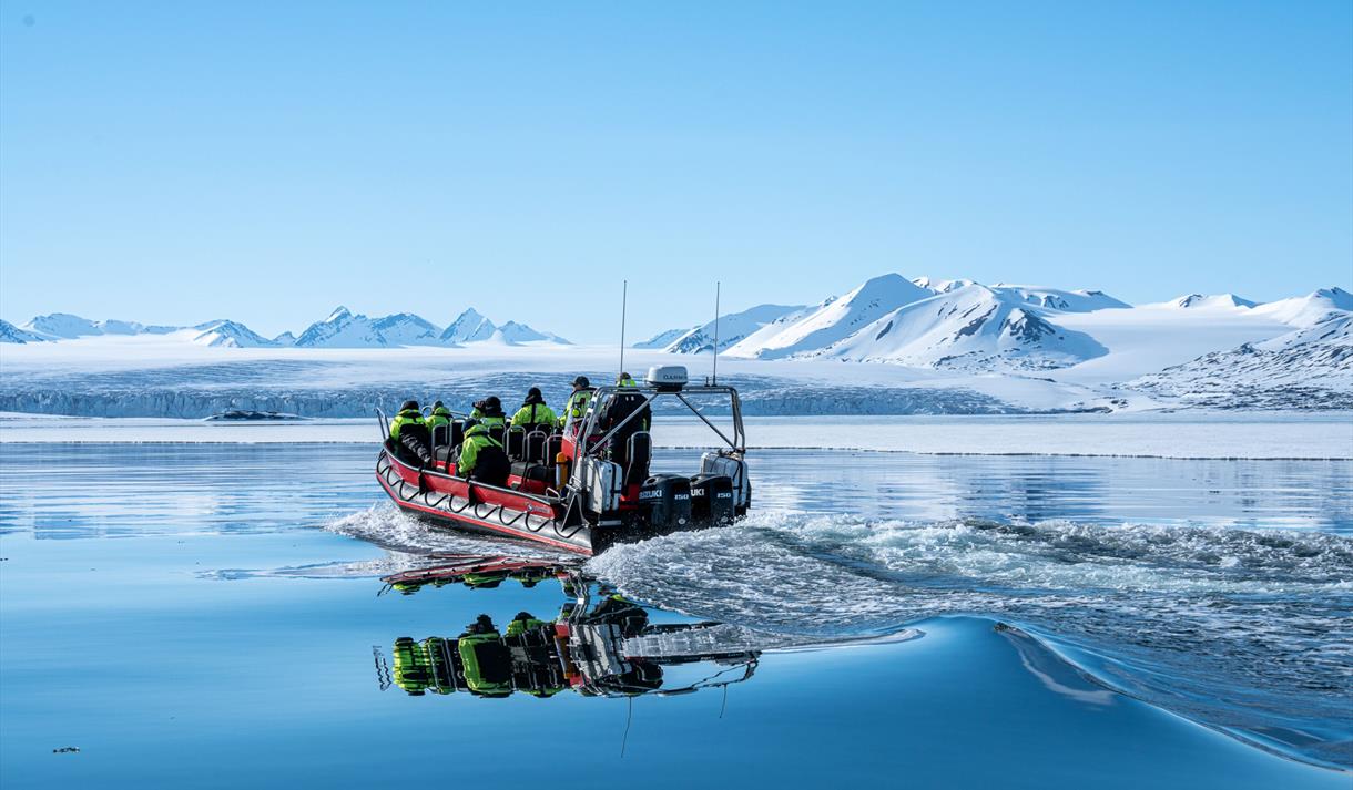 An open RIBboat travels through Arctic waters surrounded by snow-covered mountains.