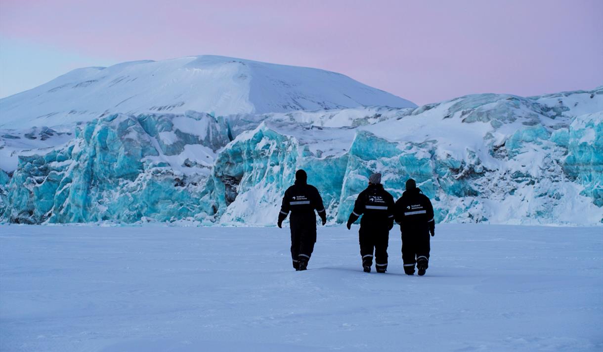 Tre personer går foran en blå isbre.