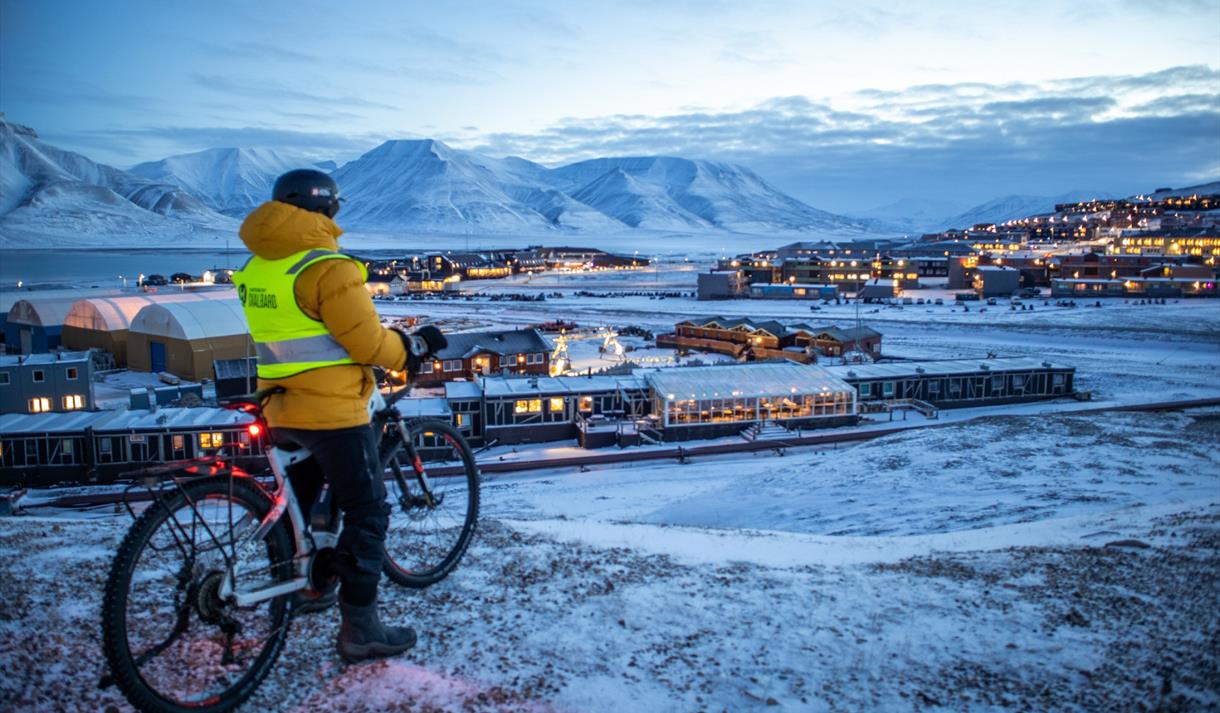 En gjest på sykkel som ser ut over bygningene i Longyearbyen fra et utsiktspunkt