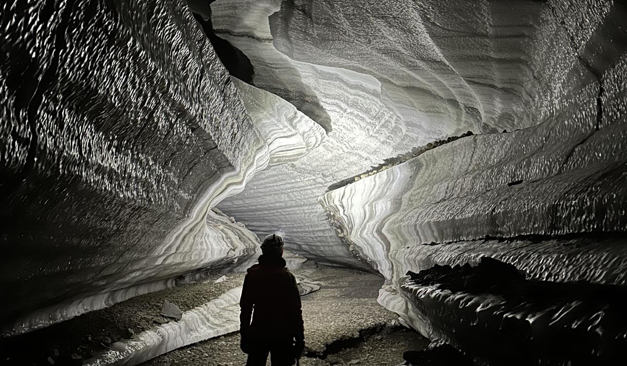 Person standing inside an ice cave with a head lamp