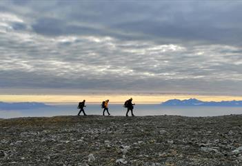 Tre personer vandrer langs kysten