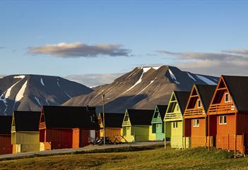 Fargerike spisse hus i forgrunnen med et fjellandskap og en lett skyet blå himmel i bakgrunnen