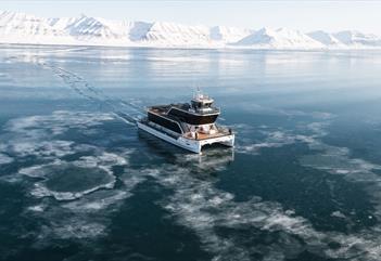 A boat (MS Bard) sailing through thin drift ice on a fjord with mountains in the background