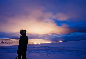 Person standing in front, on a dark winter day with the lights from town in the background