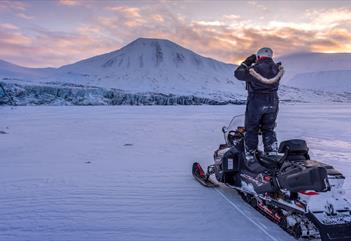 A guide standing on a snowmobile scouting out the terrain using binoculars