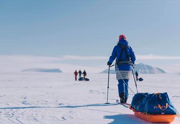 A skier pulling a sled in the foreground, with three skiers in the distance in the background