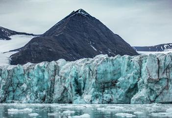 En fjord med flytende isbiter og en brefront som stiger opp mot fjell i bakgrunnen