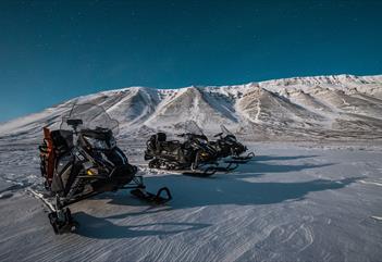 Three snowmobiles out in the wilderness beneath starry skies
