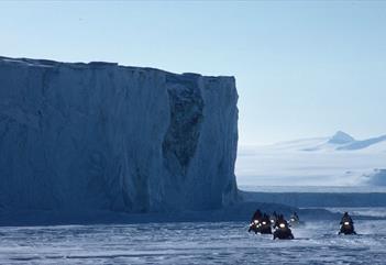 A tour group on snowmobiles with an ice wall in the background