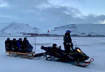 A guide driving a snowmobile with guests on the sled being pulled behind