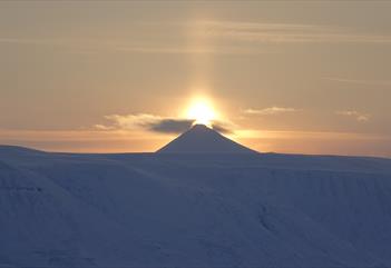 The midnight sun shining behind a mountain peak