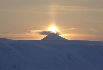 Midnattssola som skinner bak en fjelltopp