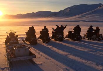 En turgruppe på snøscootere som ser mot sola