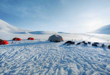 A winter landscape with tents set up on the snow under a clear sky.