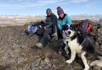 Two persons and a dog relaxing on top of a mountain