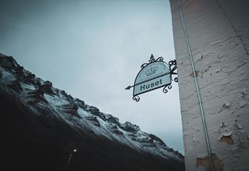 A sign next to the entrance to Huset with mountains in the background