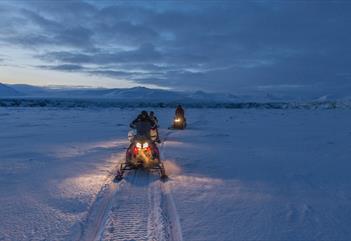 persons driving snowmobiles in a visually blue and snowcovered landscape