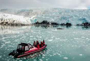 En båt med gjester om bord som seiler foran en isbre