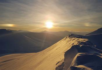 The sun shines on the snow-covered mountain top with beautiful snow-covered mountains in the back ground