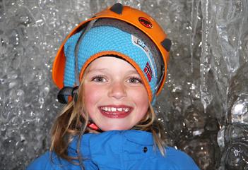 Glad og smilende barn med hjelm, inne i isgrotta