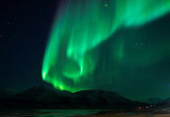 Nordlys som skinner på himmelen med mørke fjell i bakgrunnen