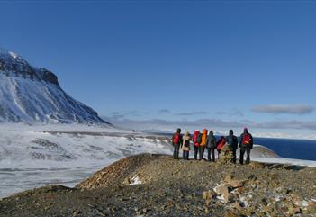 People on a small mountain looking out in the nature with snowcovered grounds and mountain in the background