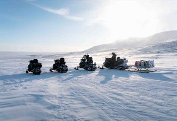 Fire snøscootere står parkert i et hvitt og snødekt landskap