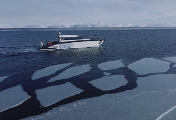 A boat sailing along sheets of ice floating on a fjord, with snow-covered mountains far away in the background