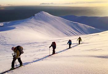 Fire personer som går på ski opp et fjell i vårsolen