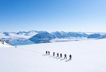 A group of people walking up a mountain on skis